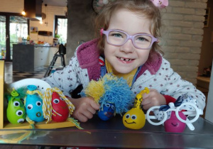 dziewczynka w okularach a przed nią na stole kolrowe ludziki wykonane z kolorowych balonów i włóczki
